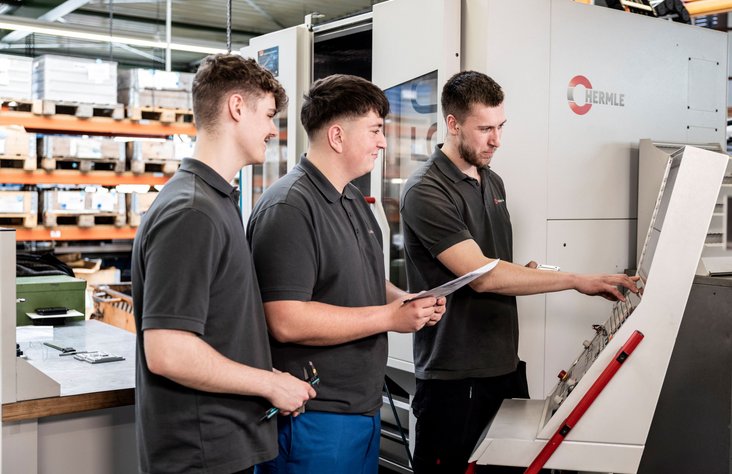 Drei Auszubildende stehen an Maschine in der Produktion von Kern Antriebstechnik
