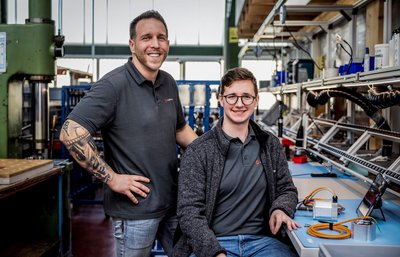 Ausbilder steht neben Azubi in der Produktion und lächelt